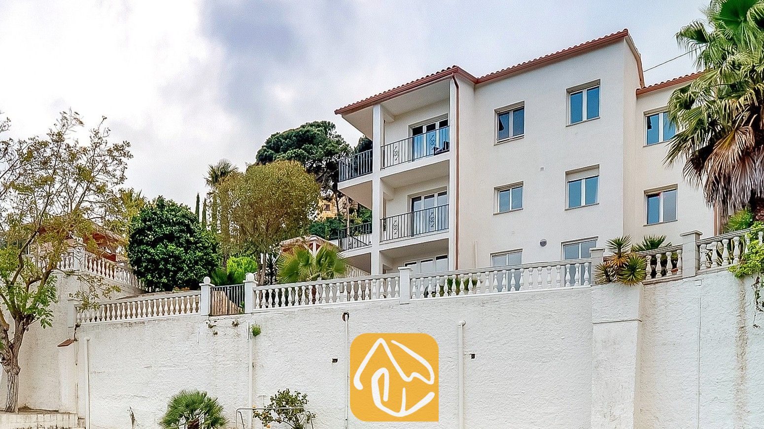 Vakantievilla's Costa Brava Spanje - Villa Tropicana - Buitenaanzicht van Villa Tropicana met een wit gebouw van meerdere verdiepingen, balkons, een pannendak van terracotta en steunmuren.