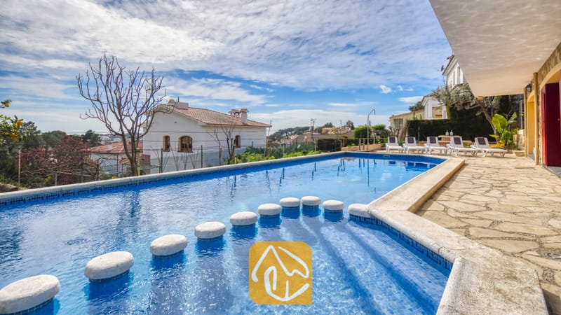 Vakantievilla's Costa Brava Spanje - Villa Janet - Rechthoekig zwembad met stapstenen en een blauw tegelinterieur bij Villa Janet in Spanje, voorzien van een stenen terras en uitzicht op de omliggende buurt onder een bewolkte blauwe hemel.