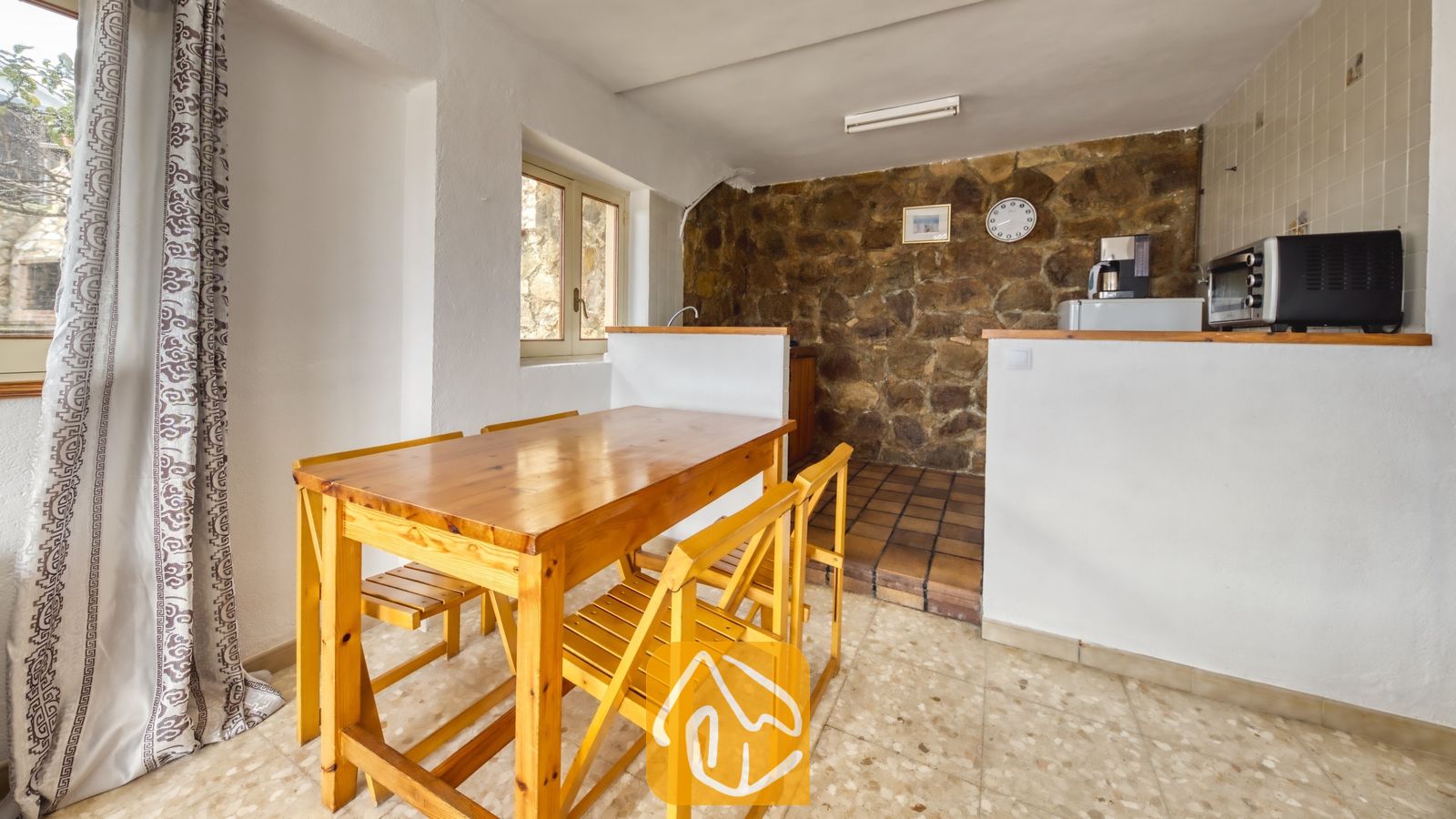 Vakantievilla's Costa Brava Spanje - Villa Janet - Houten eettafel met bijpassende stoelen in een binnenruimte met een rustieke stenen accentmuur en tegelvloer bij Villa Janet.