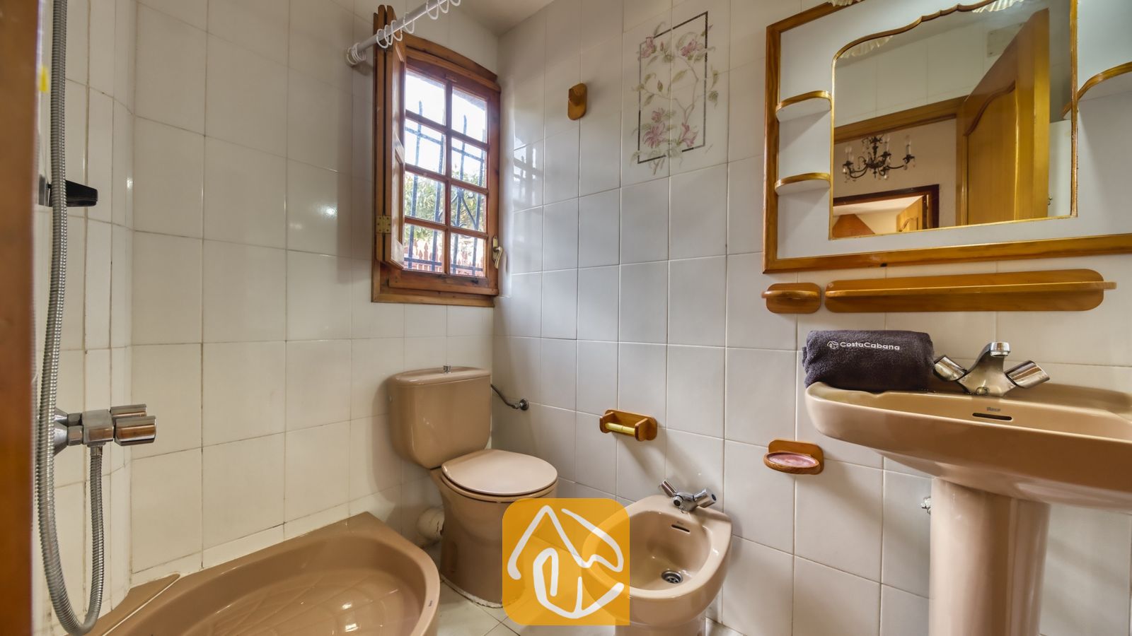 Vakantievilla's Costa Brava Spanje - Villa Janet - Badkamer met beige sanitair, bestaande uit een toilet, bidet en een wastafel met zuil, gecombineerd met witte wandtegels en een houten spiegel.