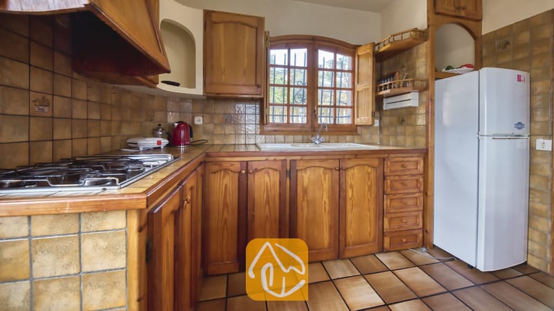 Vakantievilla's Costa Brava Spanje - Villa Janet - Traditionele, rustieke keuken met houten kasten, beige betegelde muren, een gaskookplaat en een witte koelkast.
