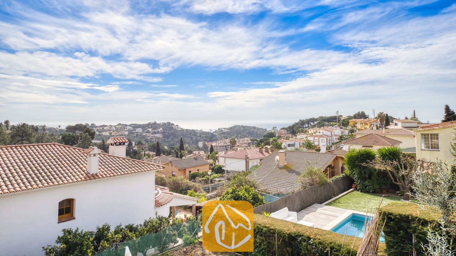 Vakantievilla's Costa Brava Spanje - Villa Janet - Een verheven uitzicht vanaf Villa Janet over terracotta dakpannen, groene heuvels en een zwembad beneden onder een blauwe lucht.