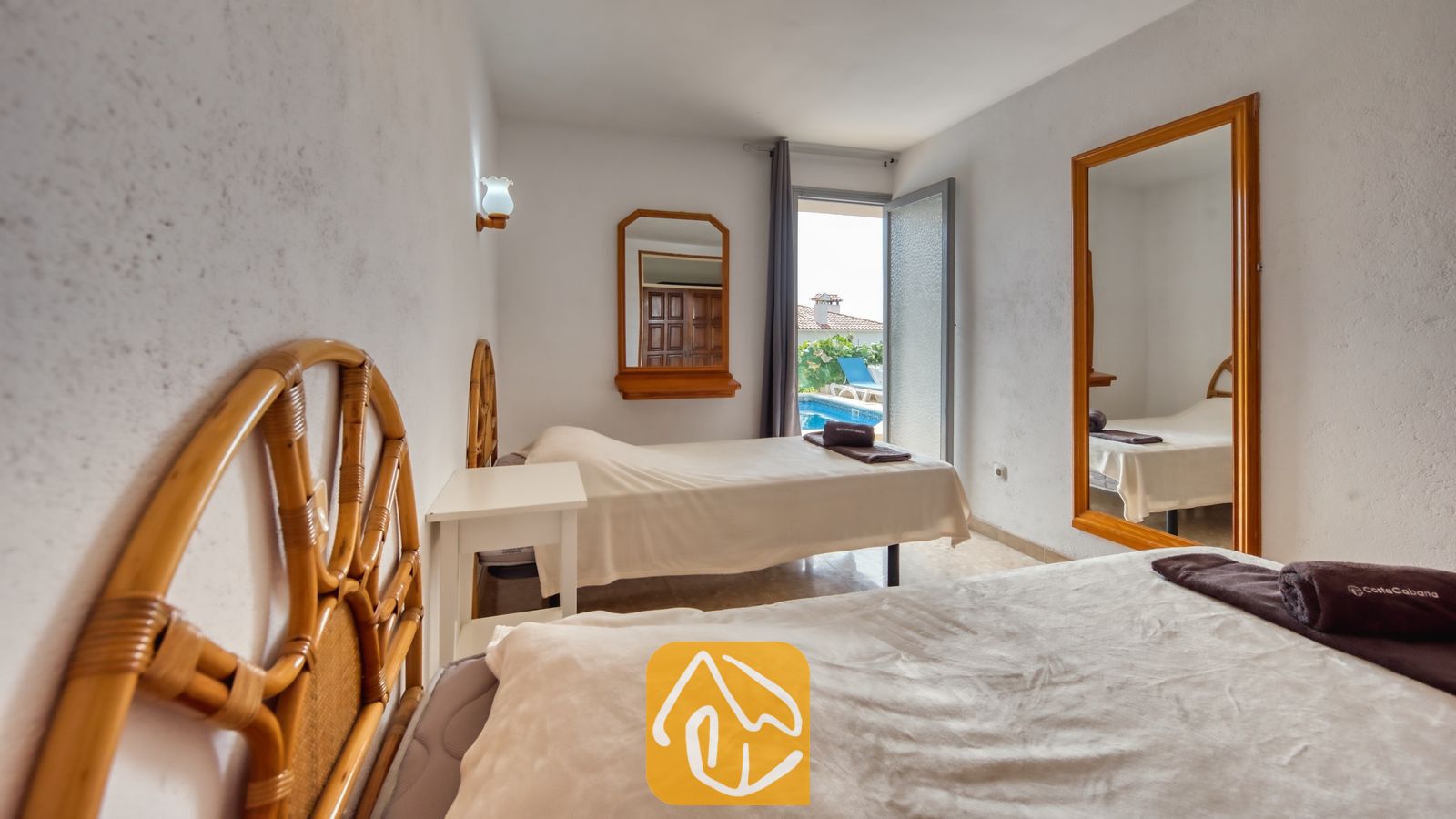 Vakantievilla's Costa Brava Spanje - Villa Janet - Slaapkamer met twee eenpersoonsbedden, houten hoofdborden, wit beddengoed en een deuropening die leidt naar een uitzicht op het zwembad.