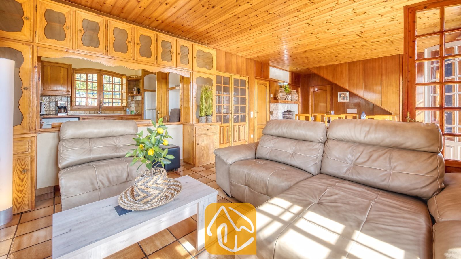 Vakantievilla's Costa Brava Spanje - Villa Janet - Interieur van de woonkamer in Villa Janet met houten wanden en plafonds, bruine leren banken en een witte salontafel met een klein potje met een citroenboompje.