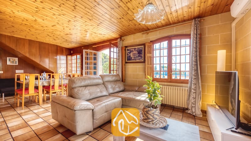 Vakantievilla's Costa Brava Spanje - Villa Janet - Woonkamer van Villa Janet met een beige lederen hoekbank, houten paneelplafonds, een tegelvloer en een eethoek op de achtergrond.