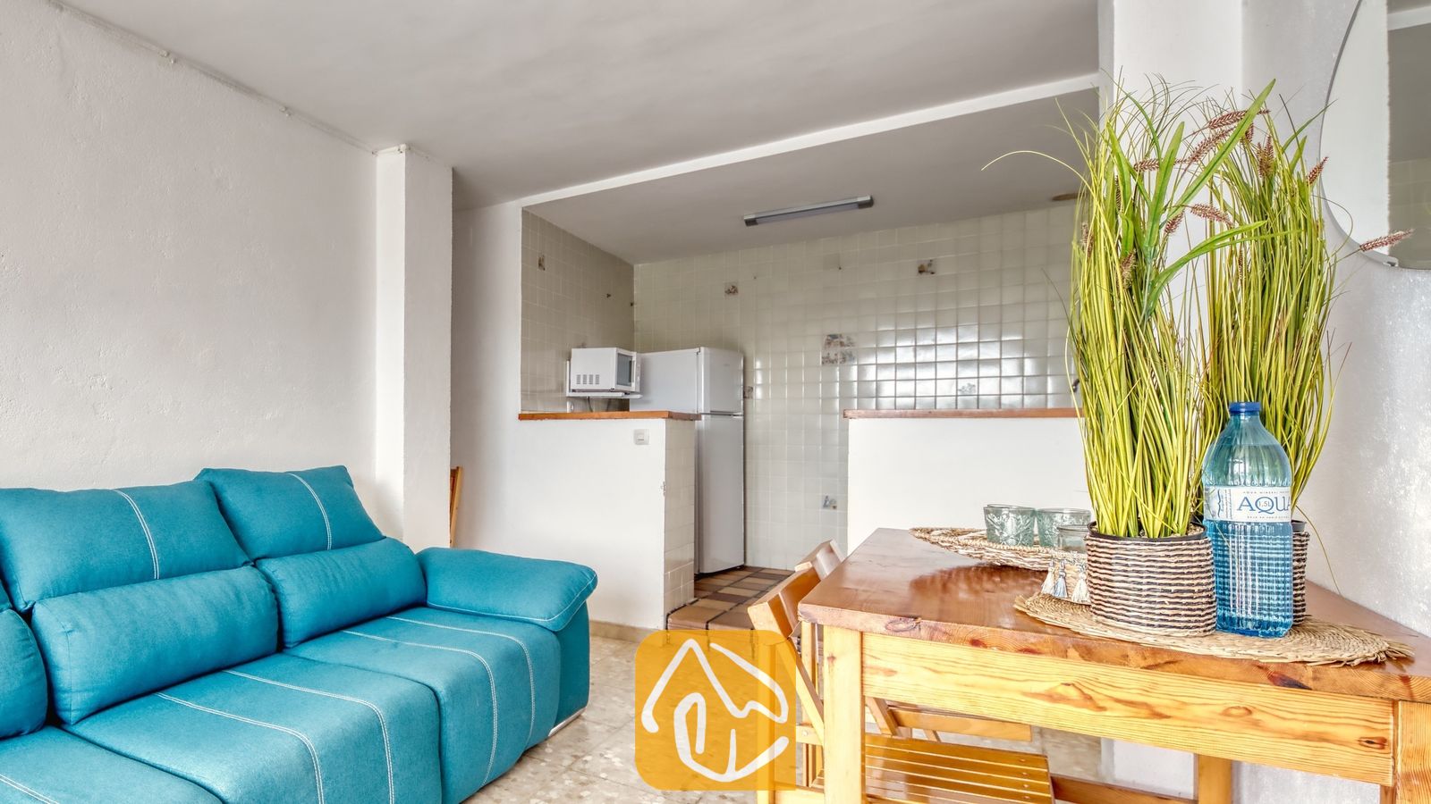 Vakantievilla's Costa Brava Spanje - Villa Janet - Lichte woonkamer met een blauwe bank en een houten eettafel, voorzien van een plant in pot en een waterfles.