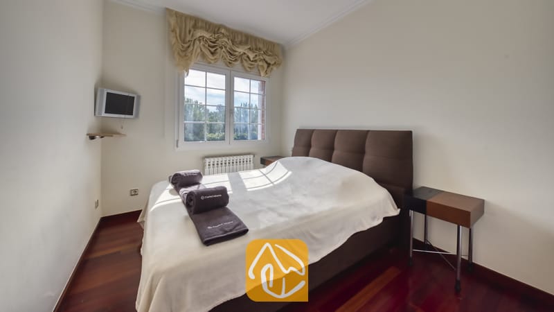 Vakantievilla's Costa Brava Spanje - Villa Beyonce - Slaapkamer met een bruin gestoffeerd tweepersoonsbed, opgevouwen grijze handdoeken, wit beddengoed en twee houten nachtkastjes op een donkere houten vloer.