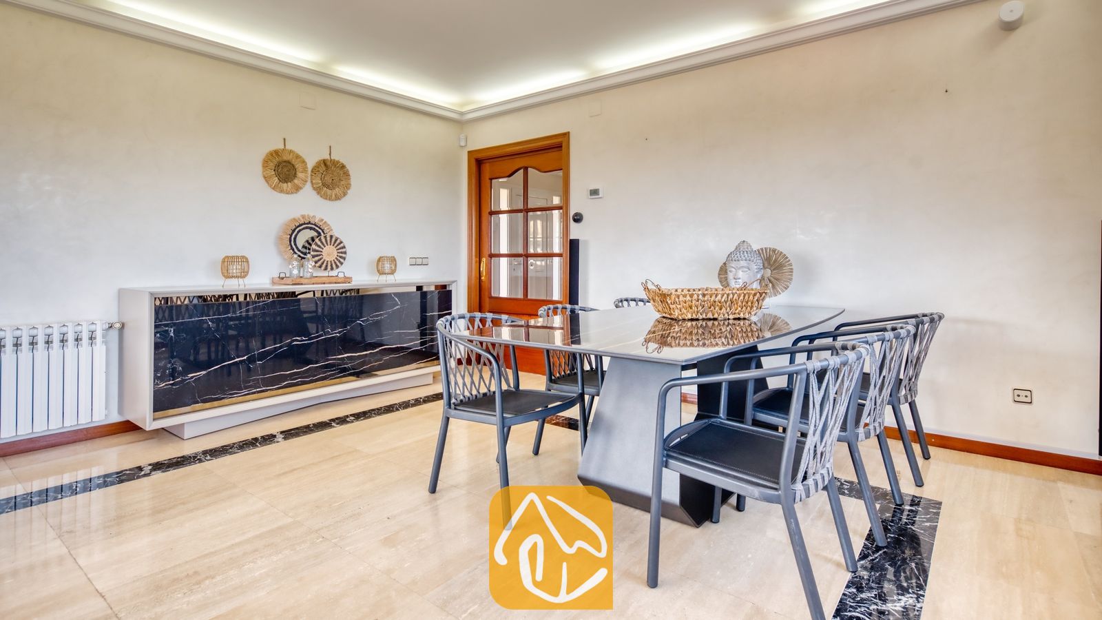 Vakantievilla's Costa Brava Spanje - Villa Beyonce - Eetkamer met een zwart marmeren tafel, bijpassende donkere stoelen met rugleuningen van geweven touw en een harmonieus dressoir in Villa Beyonce.