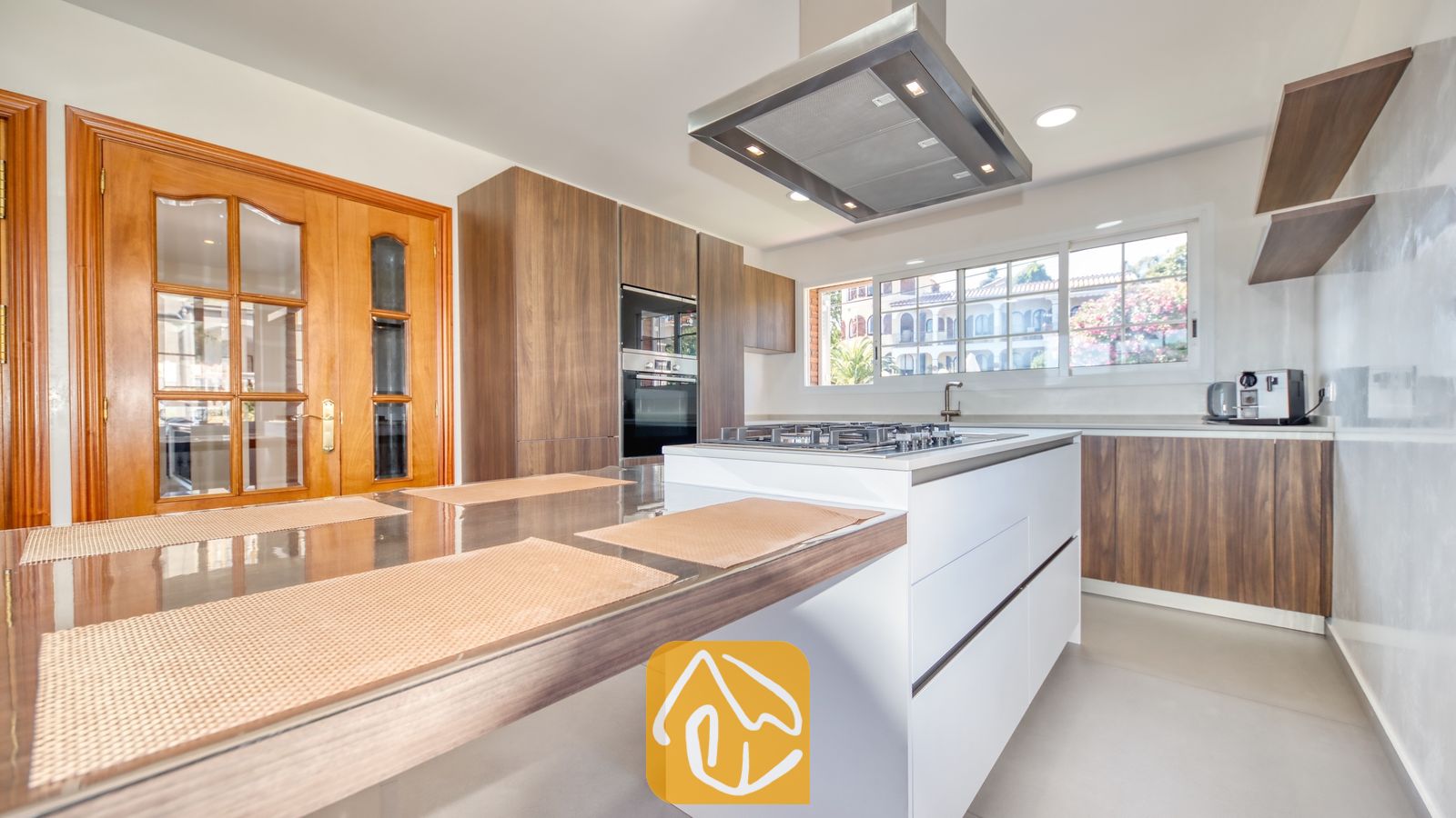 Vakantievilla's Costa Brava Spanje - Villa Beyonce - Moderne keuken met houten kasten, een wit eiland met een geïntegreerd gasfornuis en daarboven een grote RVS afzuigkap.