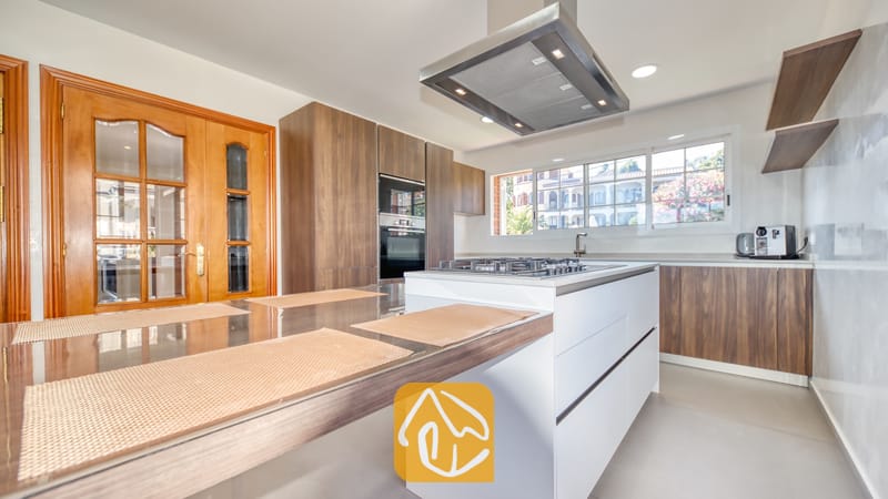 Vakantievilla's Costa Brava Spanje - Villa Beyonce - Moderne keuken met houten kasten, een wit eiland met een geïntegreerd gasfornuis en daarboven een grote RVS afzuigkap.