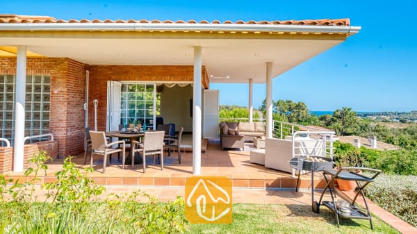 Vakantievilla's Costa Brava Spanje - Villa Beyonce - Overdekt terras bij Villa Beyonce met een eethoek buiten, een loungesofa, een verplaatsbare grill en rode bakstenen buitenmuren onder een blauwe lucht.