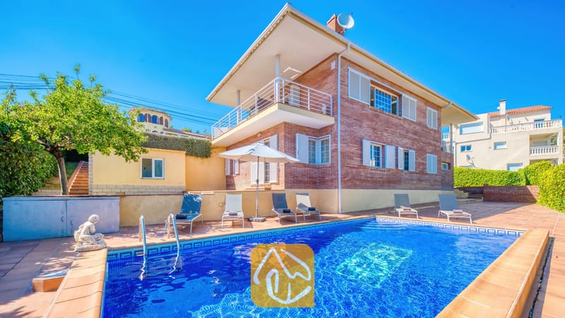 Vakantievilla's Costa Brava Spanje - Villa Beyonce - Buitenaanzicht van Villa Beyonce met een rechthoekig zwembad met blauwe tegels, ligstoelen en een stenen gebouw van twee verdiepingen onder een helderblauwe hemel