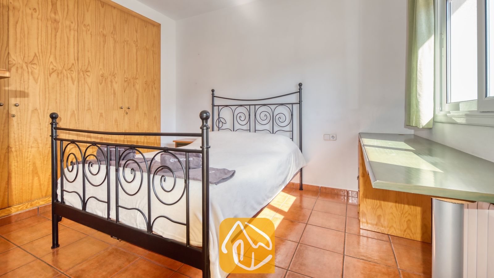 Vakantievilla's Costa Brava Spanje - Villa Valeria - Slaapkamer met een zwart metalen bed, rode plavuizen en een grote houten kledingkast.
