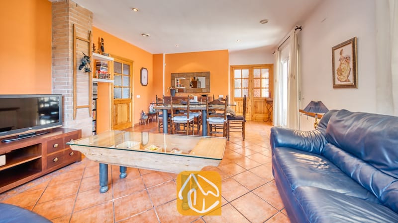 Vakantievilla's Costa Brava Spanje - Villa Valeria - Ruime woon- en eetkamer in Villa Valeria met oranje muren, terracotta plavuizen, een blauwe leren bank en een houten eettafel met bijpassende stoelen.