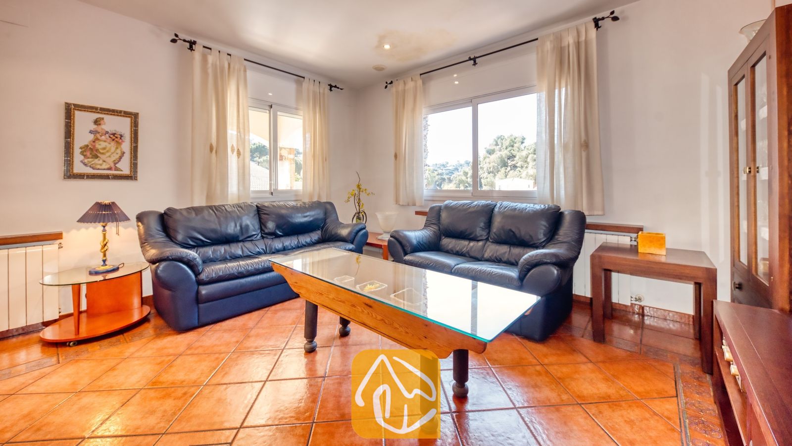 Vakantievilla's Costa Brava Spanje - Villa Valeria - Woonkamer met twee donkere leren banken, een houten salontafel met glazen blad en terracotta plavuizen.