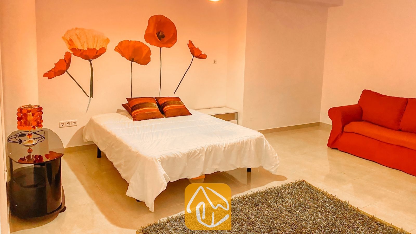 Vakantievilla's Costa Brava Spanje - Villa Primavera - Slaapkamer met een tweepersoonsbed, voorzien van wit beddengoed, rood gestreepte kussens en een grote muurschildering van een klaproos boven het hoofdeinde.