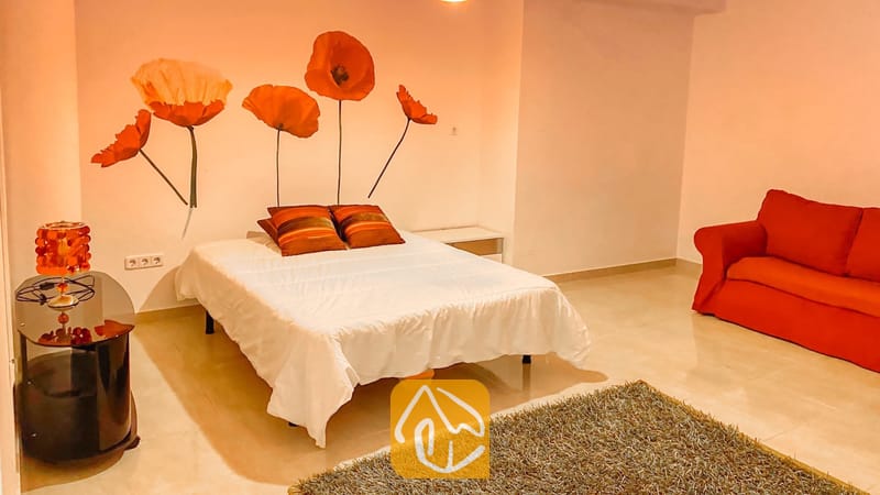 Villas de vacances Costa Brava Espagne - Villa Primavera - Chambre à coucher dotée d'un lit double avec des draps blancs, des oreillers à rayures rouges et une grande fresque murale représentant un coquelicot au-dessus de la tête de lit.