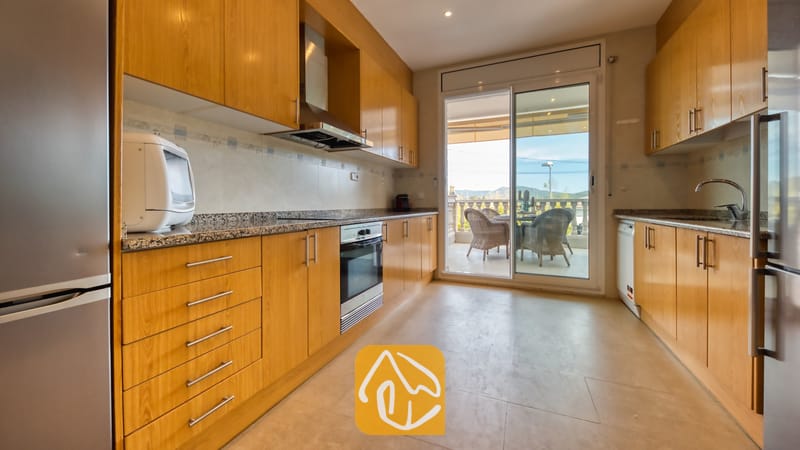 Vakantievilla's Costa Brava Spanje - Villa Primavera - Interieur van de keuken in Villa Primavera met houten kasten, granieten aanrechtbladen en glazen schuifdeuren die uitkomen op een terras.