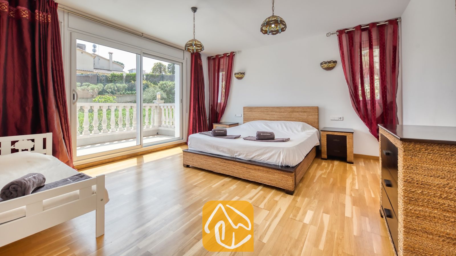 Vakantievilla's Costa Brava Spanje - Villa Primavera - Slaapkamer in Villa Primavera met een groot tweepersoonsbed met gevlochten rattan frame, houten vloer en glazen schuifdeuren die opengaan naar een terras.
