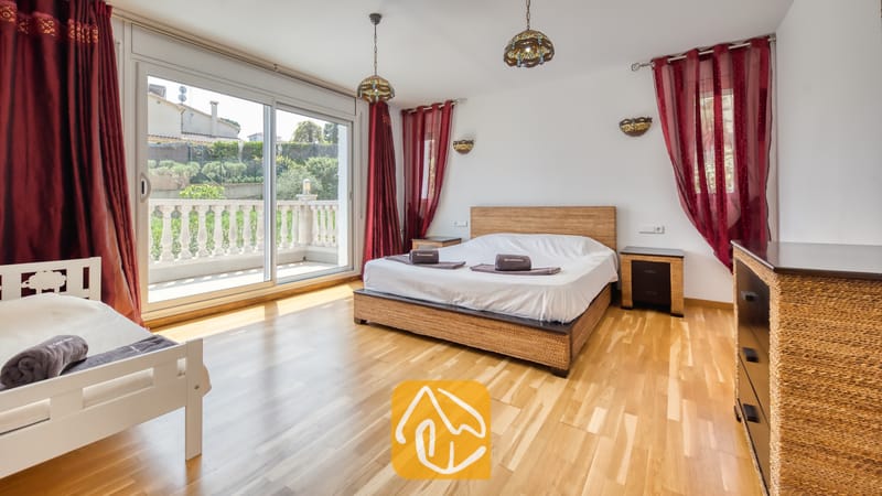 Villas de vacances Costa Brava Espagne - Villa Primavera - Chambre de la Villa Primavera dotée d'un grand lit double avec un cadre en rotin tressé, d'un parquet et de baies vitrées coulissantes s'ouvrant sur une terrasse.