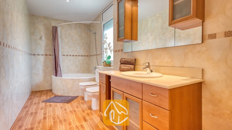 Villas de vacances Costa Brava Espagne - Villa Primavera - Salle de bain comprenant un meuble sous-lavabo en bois avec tiroirs, une baignoire aux lignes courbes avec rideau de douche, et des murs carrelés de beige.