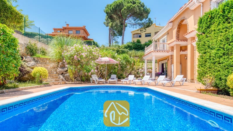 Vakantievilla's Costa Brava Spanje - Villa Primavera - Privézwembad met blauwe tegelrand en witte ligstoelen op het terras van Villa Primavera, prachtig af tegen een perzikleurige buitenmuur en weelderig tuingroen.