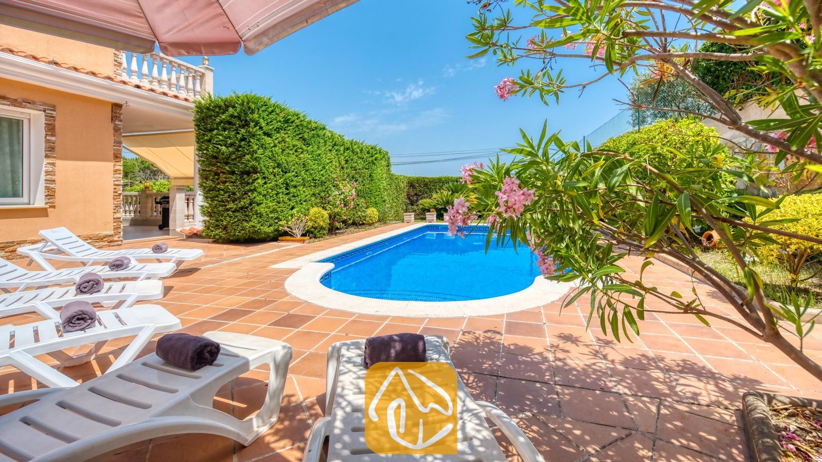 Vakantievilla's Costa Brava Spanje - Villa Primavera - Privé-buitenzwembad bij Villa Primavera, omringd door een betegeld terras, witte ligstoelen met opgerolde donkere handdoeken en bloeiende takken van roze oleanders.