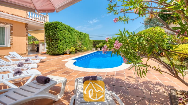 Vakantievilla's Costa Brava Spanje - Villa Primavera - Privé-buitenzwembad bij Villa Primavera, omringd door een betegeld terras, witte ligstoelen met opgerolde donkere handdoeken en bloeiende takken van roze oleanders.