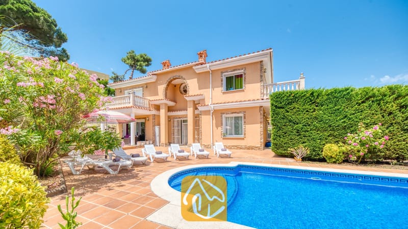 Vakantievilla's Costa Brava Spanje - Villa Primavera - Privézwembad en terras bij Villa Primavera, voorzien van witte ligstoelen, terracotta tegels en een perzikleurige buitenkant van twee verdiepingen onder een blauwe hemel.