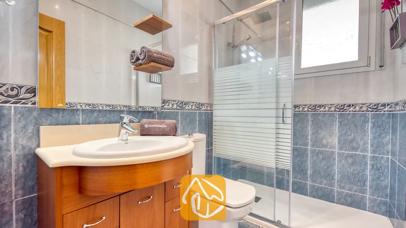 Villas de vacances Costa Brava Espagne - Villa Primavera - Salle de bains moderne dotée de murs carrelés de bleu, d'un meuble sous-vasque en bois avec vasque blanche, de toilettes et d'une douche vitrée.