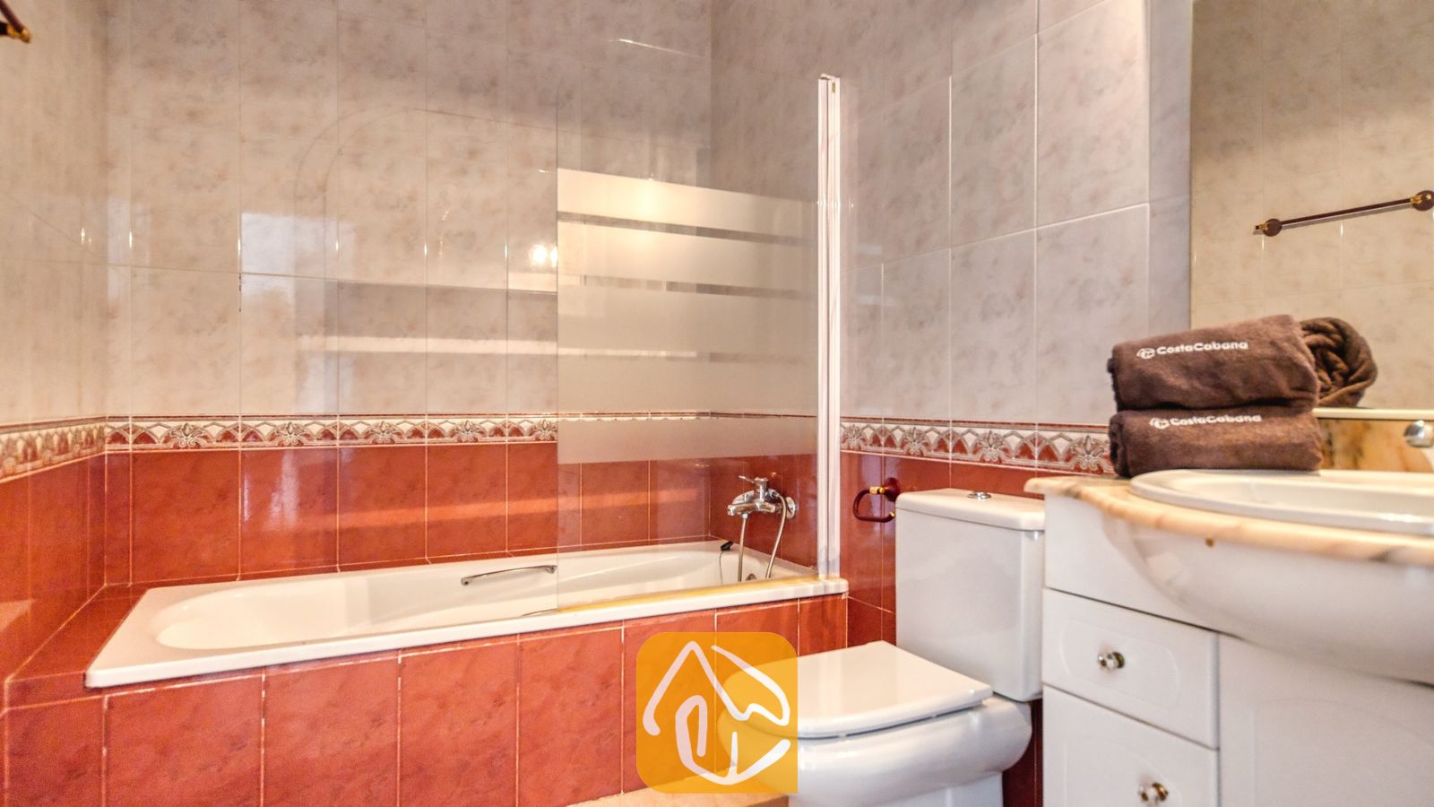 Vakantievilla's Costa Brava Spanje - Villa Sunrise - Badkamer voorzien van een ligbad met een glazen scherm, een wit toilet en een wastafelmeubel met opgevouwen bruine handdoeken.