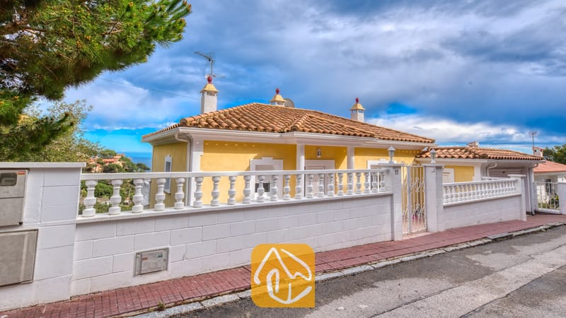 Holiday villas Costa Brava Spain - Villa Sunrise - Exterior view of Villa Sunrise showing its yellow facade, terracotta tile roof, and a white balustrade fence along the street.