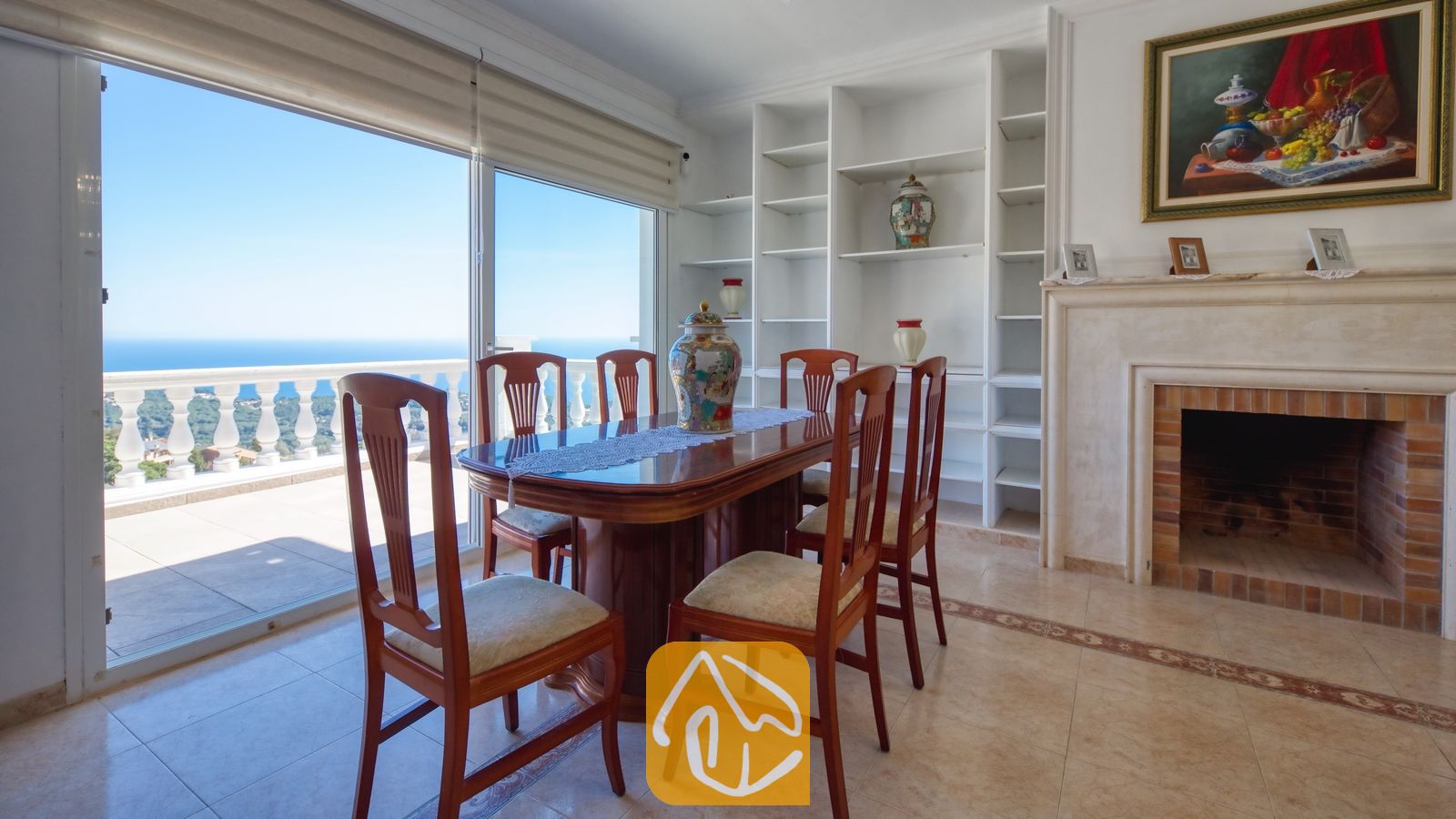 Vakantievilla's Costa Brava Spanje - Villa Sunrise - Eethoek met een gepolijste houten tafel en gestoffeerde stoelen naast een glazen schuifpui die uitkomt op een balkon met uitzicht op zee bij Villa Sunrise