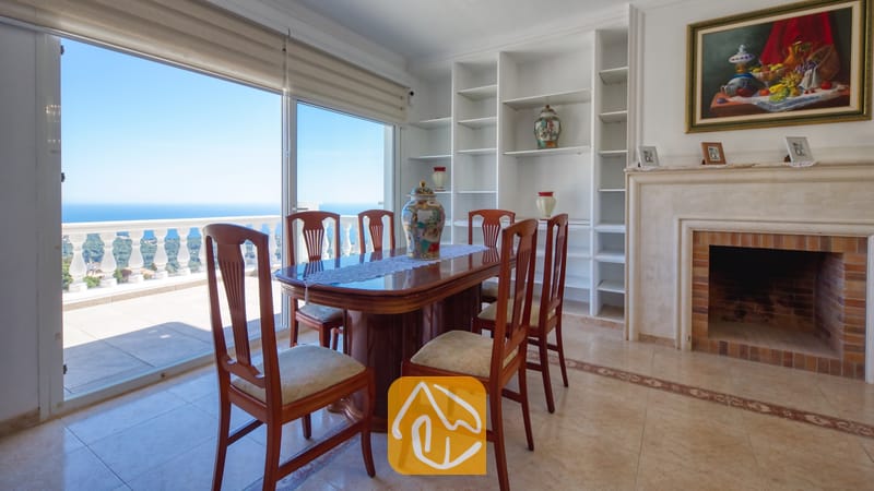 Vakantievilla's Costa Brava Spanje - Villa Sunrise - Eethoek met een gepolijste houten tafel en gestoffeerde stoelen naast een glazen schuifpui die uitkomt op een balkon met uitzicht op zee bij Villa Sunrise