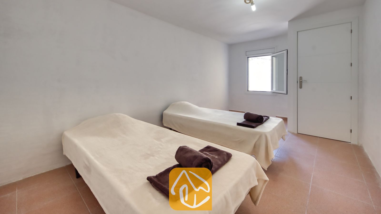 Vakantievilla's Costa Brava Spanje - Villa Sunrise - Slaapkamer met twee eenpersoonsbedden voorzien van lichte beige dekens en opgerolde bruine handdoeken erop, tegen witte muren en een tegelvloer.