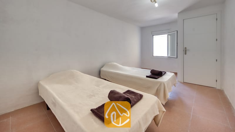 Holiday villas Costa Brava Spain - Villa Sunrise - Bedroom with two single beds covered in light beige blankets and rolled brown towels on top, set against white walls and a tiled floor.