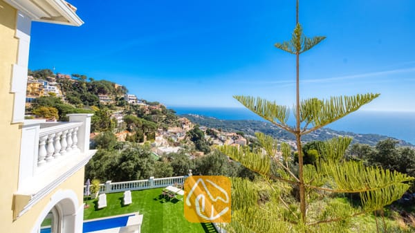 Vakantievilla's Costa Brava Spanje - Villa Sunrise - Uitzicht vanaf het balkon over de kustlijn, het stadje op de heuvel en de blauwe zee vanaf Villa Sunrise, met witte balustrades en een groene dennenboom.