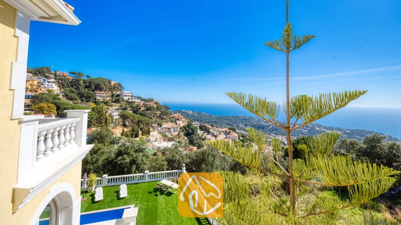 Vakantievilla's Costa Brava Spanje - Villa Sunrise - Uitzicht vanaf het balkon over de kustlijn, het stadje op de heuvel en de blauwe zee vanaf Villa Sunrise, met witte balustrades en een groene dennenboom.