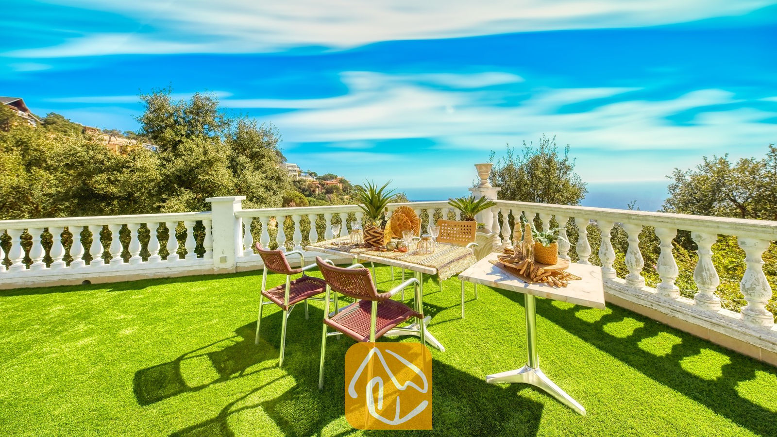 Vakantievilla's Costa Brava Spanje - Villa Sunrise - Terras met een eettafel, geweven stoelen en een witte balustrade met uitzicht op bomen en de blauwe zee bij Villa Sunrise in Spanje.