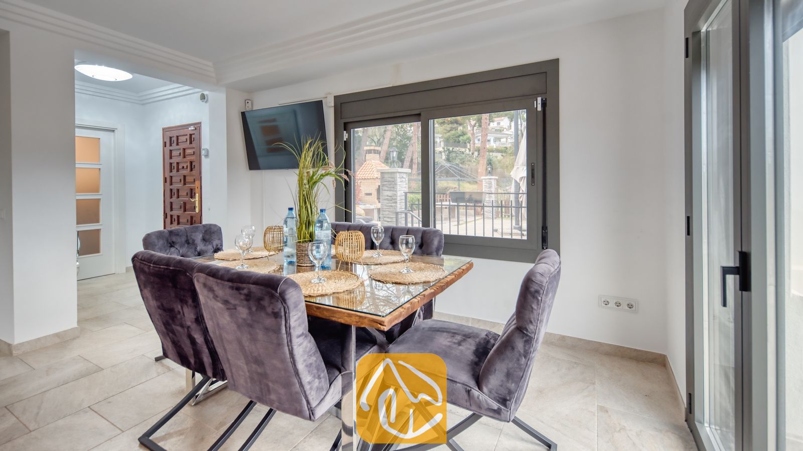 Vakantievilla's Costa Brava Spanje - Villa Palmera - Eethoek met een glazen tafel omringd door donkergrijze fluwelen stoelen, geplaatst voor een raam met uitzicht naar buiten.