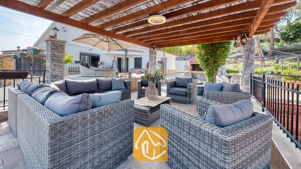 Vakantievilla's Costa Brava Spanje - Villa Palmera - Overdekt buitenterras bij Villa Palmera, voorzien van grijs rieten banken, fauteuils en een houten pergolaplafond.