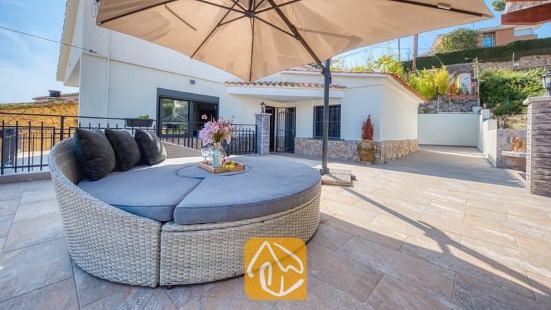 Vakantievilla's Costa Brava Spanje - Villa Palmera - Ronde, rieten buiten-daybed met grijze kussens en een grote, beige parasol op het tegelterras van Villa Palmera