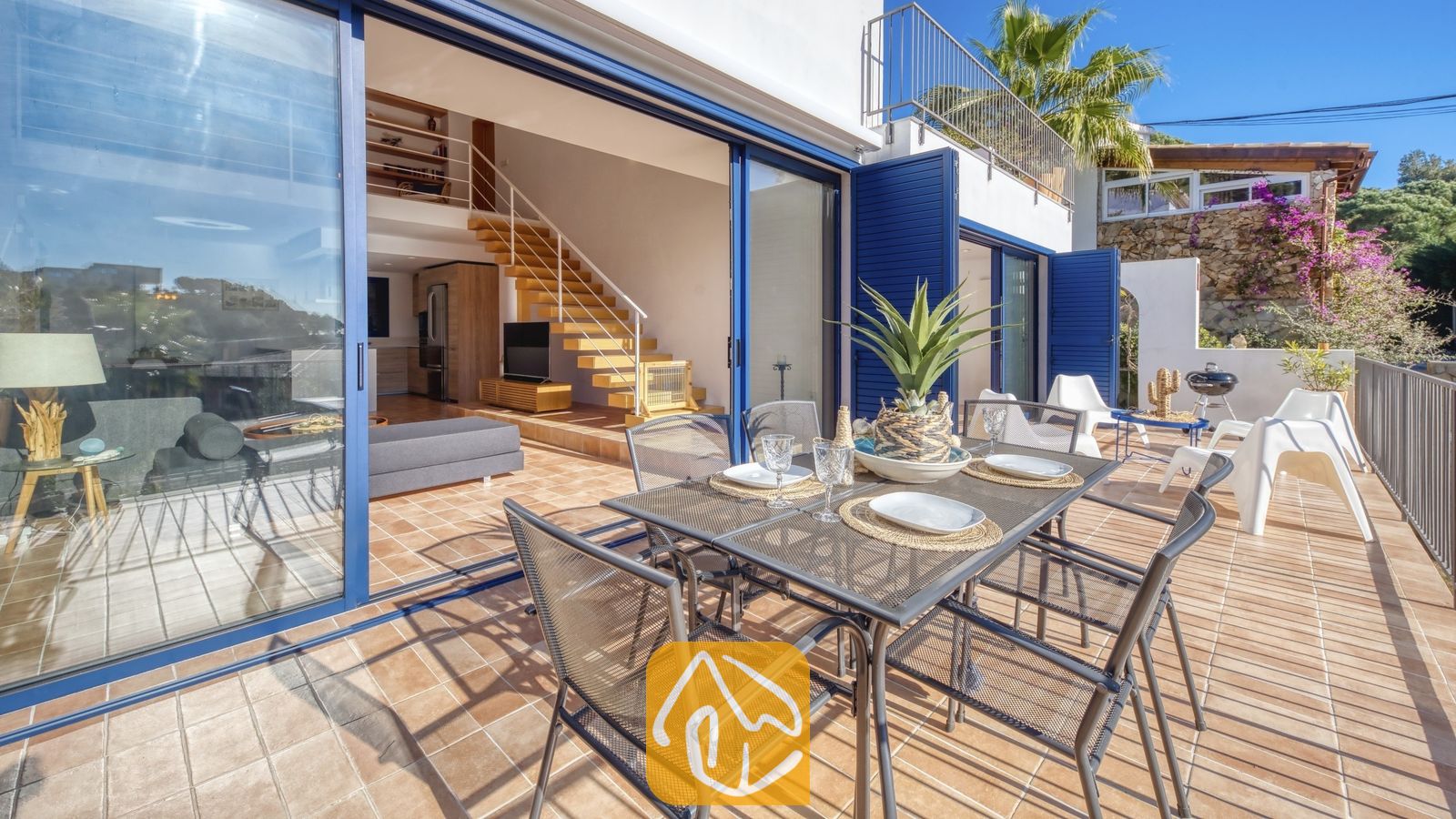 Vakantievilla's Costa Brava Spanje - Casa AdoRa - Buitenomgeving met einterras bij Casa AdoRa, voorzien van een metalen rastertafel, zes bijpassende stoelen en glazen schuifdeuren die uitkomen op een binnenwoonruimte met een houten trap.
