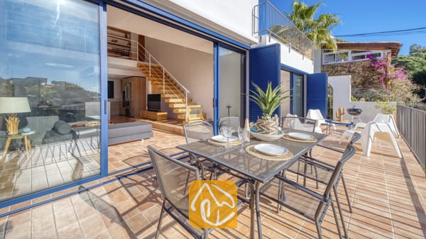 Vakantievilla's Costa Brava Spanje - Casa AdoRa - Buitenomgeving met einterras bij Casa AdoRa, voorzien van een metalen rastertafel, zes bijpassende stoelen en glazen schuifdeuren die uitkomen op een binnenwoonruimte met een houten trap.