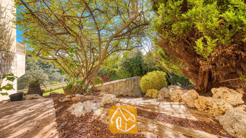 Villas de vacances Costa Brava Espagne - Villa Holiday - Allée de jardin de la Villa Holiday avec des marches en pierre bordées d'arbres matures, de grands rochers et une végétation luxuriante baignée de soleil