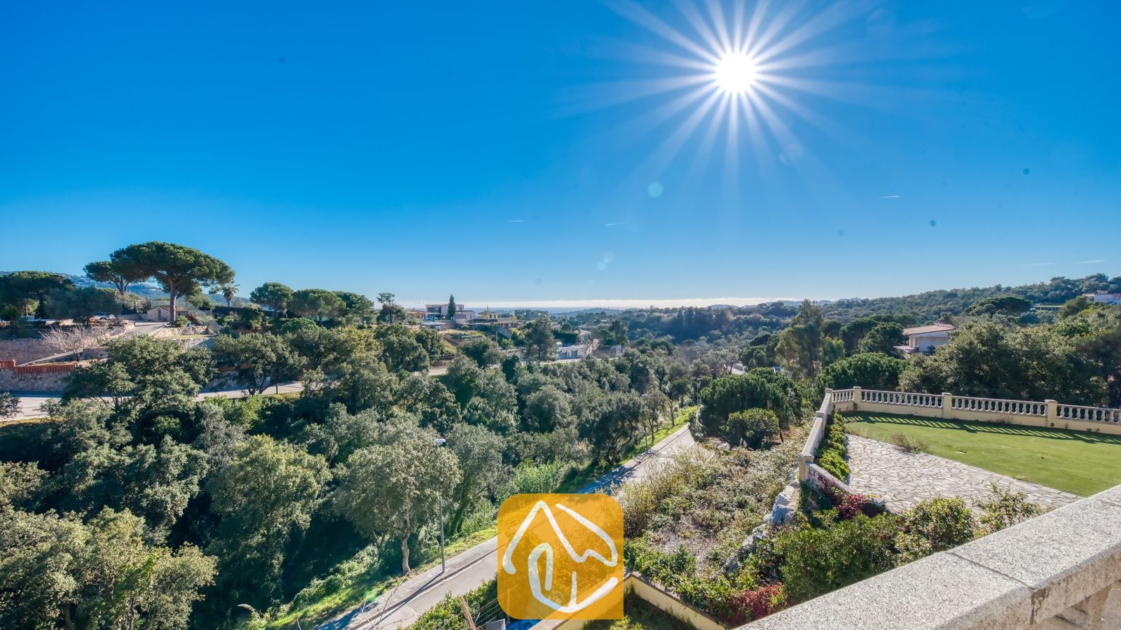 Vakantievilla's Costa Brava Spanje - Villa Holiday - Uitzicht vanaf het balkon van Villa Holiday over weelderige groene bossen, slingerende wegen en een heldere, zonnige hemel met een zichtbare zonnestraal.