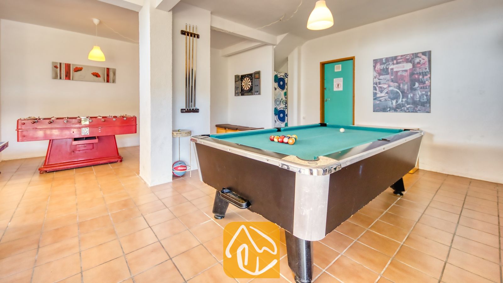 Vakantievilla's Costa Brava Spanje - Villa Holiday - Binnen-speelkamer met een groene biljarttafel op de voorgrond, een rode tafelvoetbaltafel aan de linkerkant, tegelvloeren en hangende pendelverlichting.