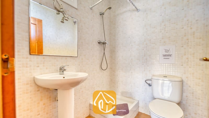 Villas de vacances Costa Brava Espagne - Villa Holiday - Salle de bains dotée de petits carreaux de mosaïque muraux beige, d'un lavabo sur pied blanc avec robinetterie en chrome, d'un miroir mural et d'une cabine de douche située à côté de toilettes blanches.
