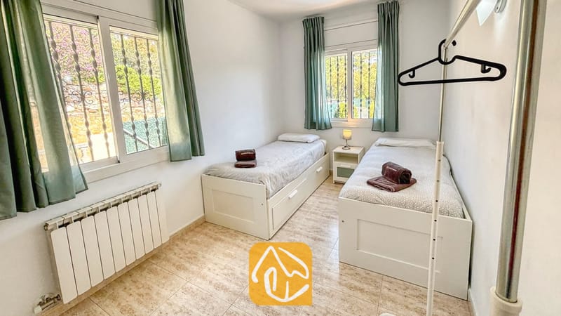 Villas de vacances Costa Brava Espagne - Villa Holiday - Chambre à lits jumeaux dotée de deux lits simples blancs, de serviettes marron enroulées, de rideaux verts et de sols carrelés.