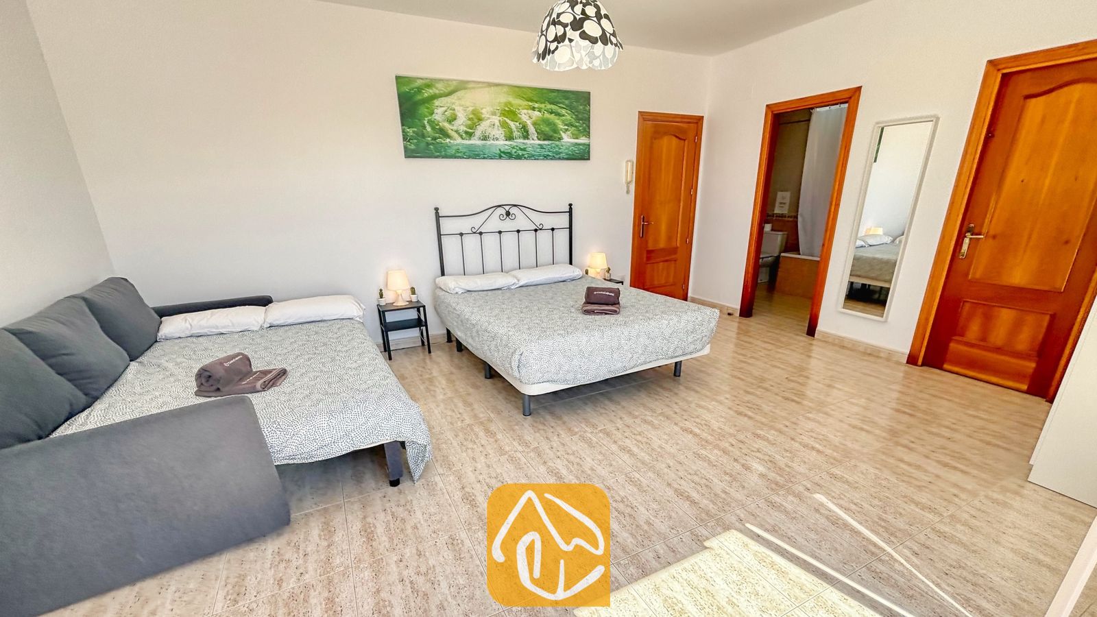 Vakantievilla's Costa Brava Spanje - Villa Holiday - Ruime slaapkamer in Villa Holiday met een tweepersoonsbed met een zwart metalen frame, een aangrenzende slaapbank voor één persoon, lichte tegelvloeren en twee houten deuren.